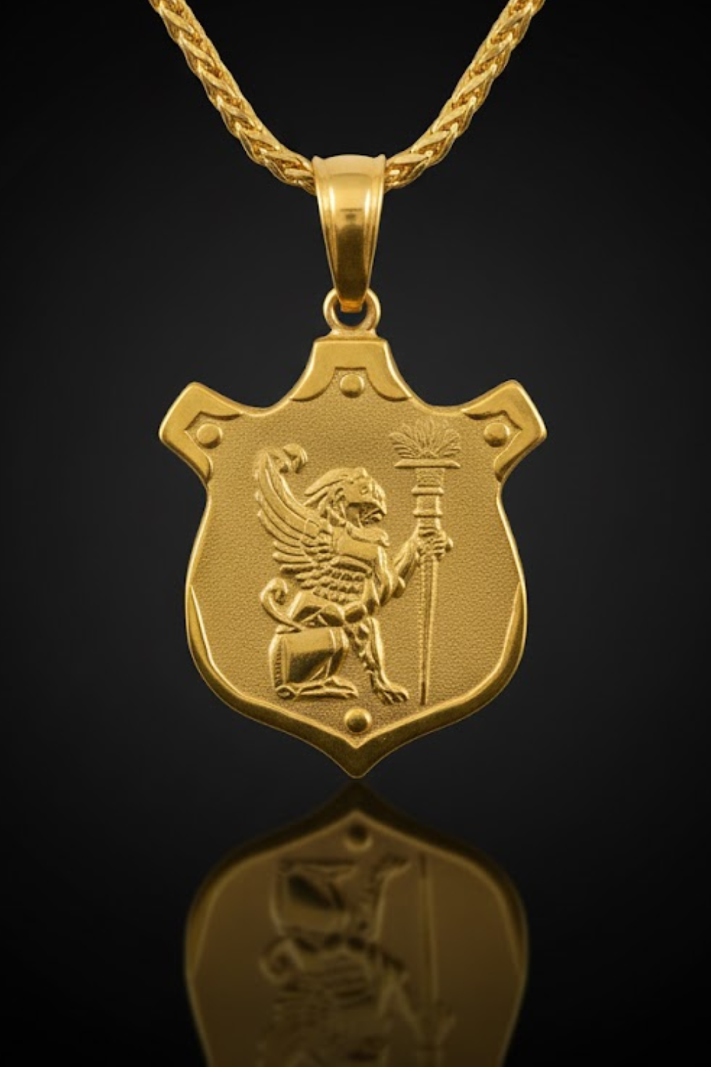 A gold-colored pendant with a shield-shaped design featuring a winged lion holding a torch, set against a dark background.