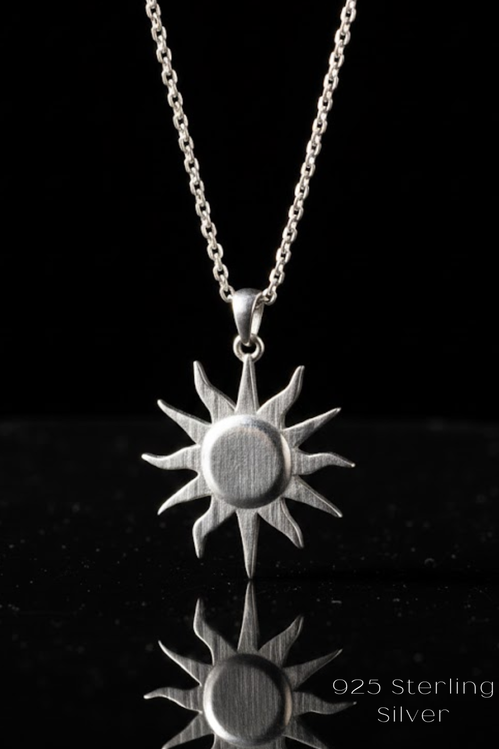 A silver pendant necklace with a sun-shaped design is displayed against a black background.