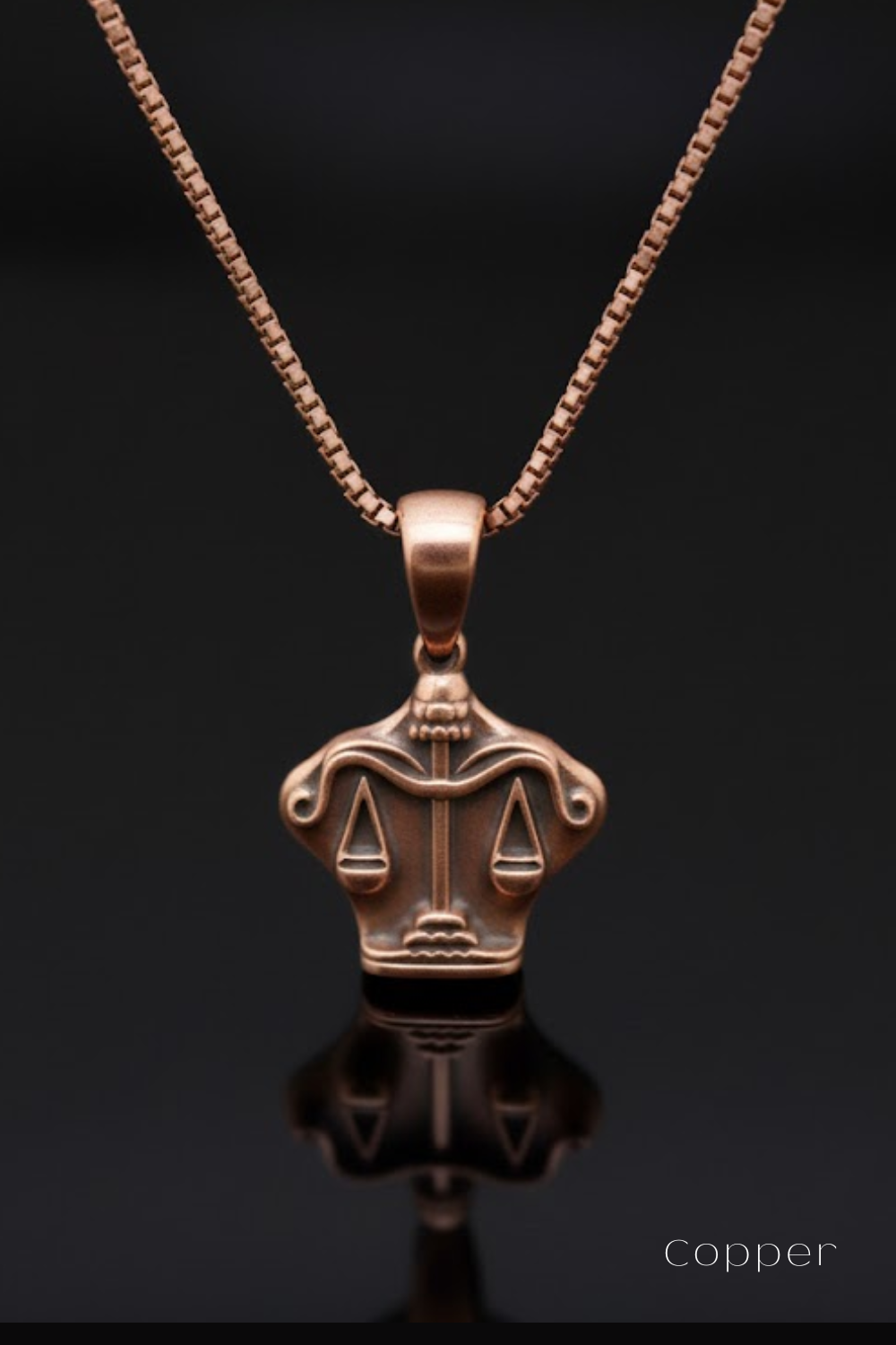A copper-colored pendant necklace with a balanced scale design on a black background.