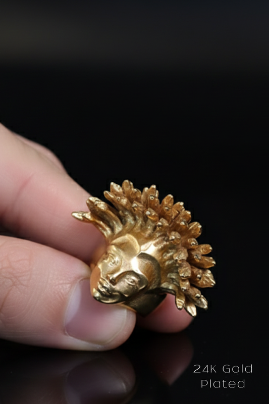 A close-up image of a person's hand holding a small, golden-colored metal object resembling a head or a face.