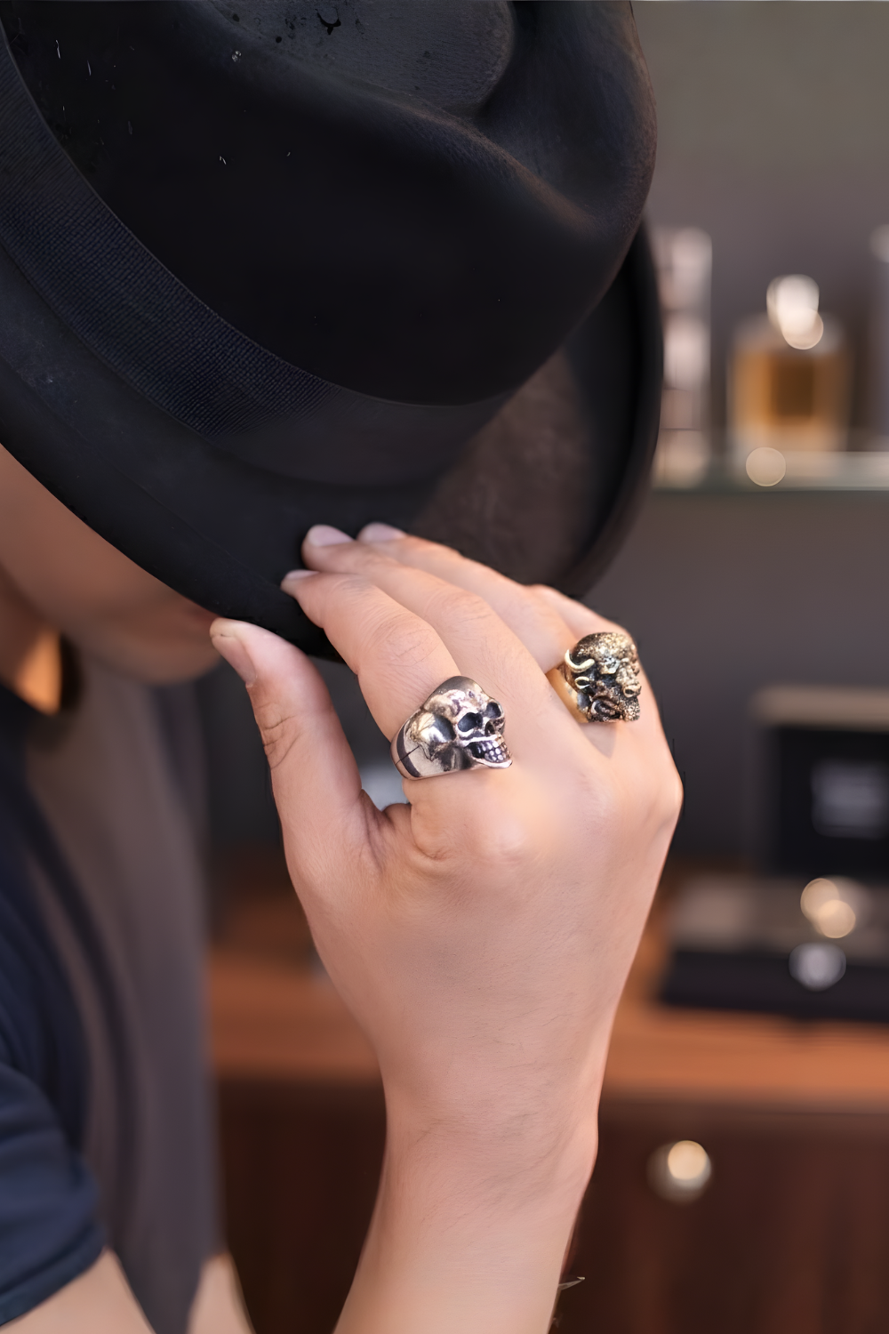 A person wearing a black hat and two skull-shaped rings is partially covering their face.