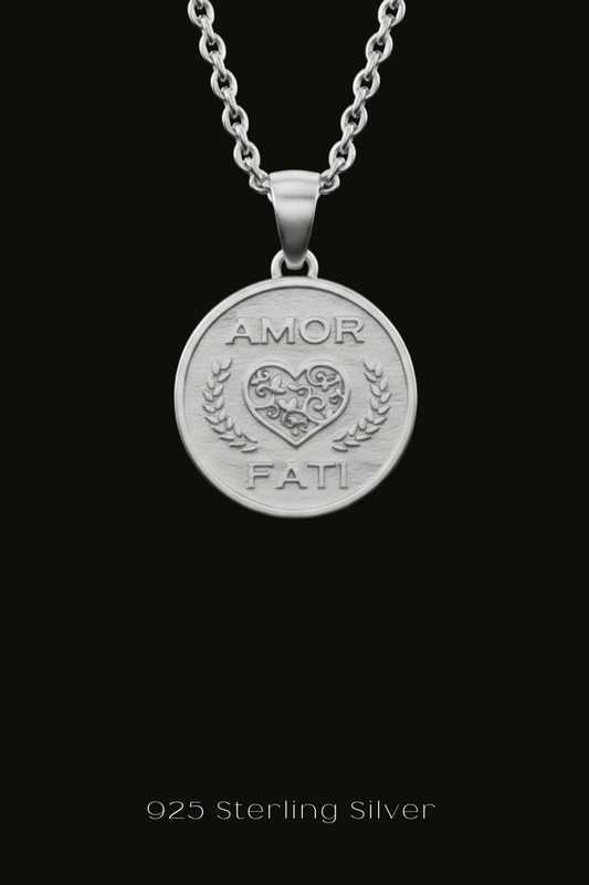 A silver pendant necklace with a heart-shaped medallion featuring the text "Amor Fati" engraved on it.