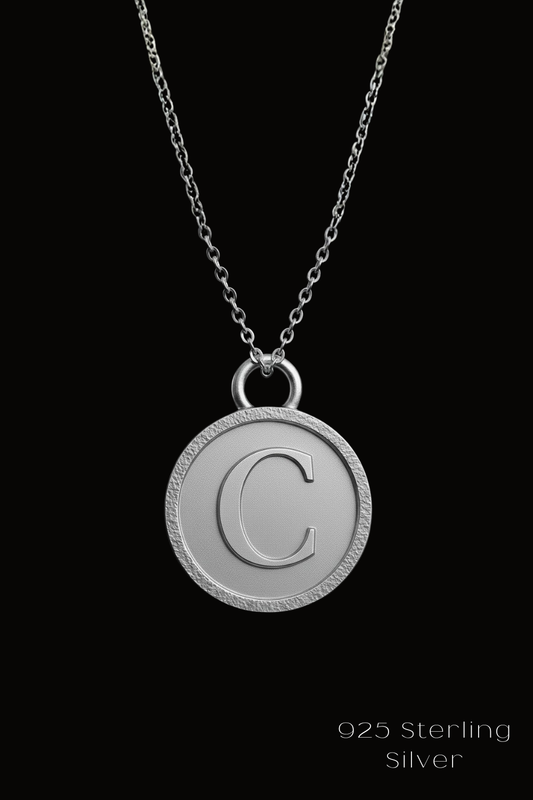 A silver necklace with a round pendant featuring the letter 'C' on a black background.