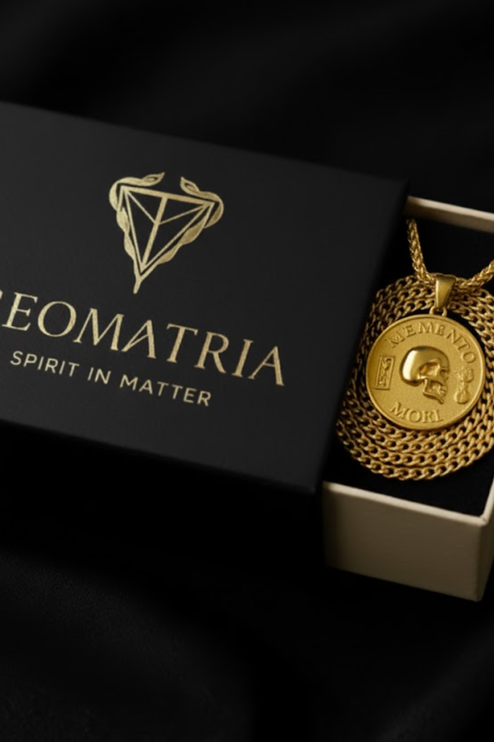 a gold necklace with a pendant, placed inside a black box with the word "Geomatria" printed on it.