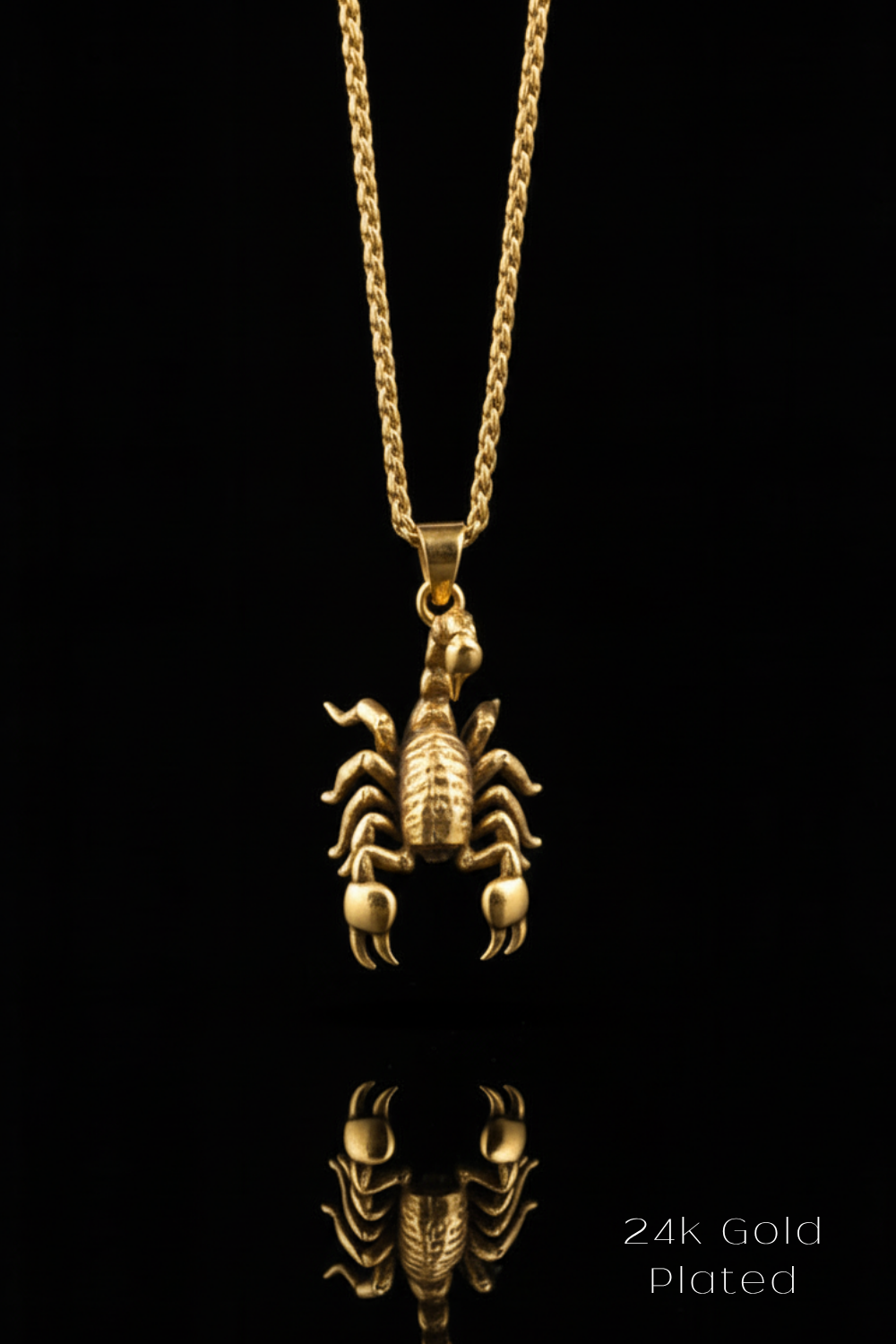 A 24k gold plated pendant in the shape of a scorpion is displayed against a black background, with its reflection visible below it.