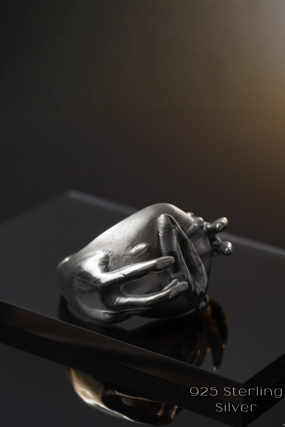 A silver ring with a unique design sits on a reflective surface against a dark background.