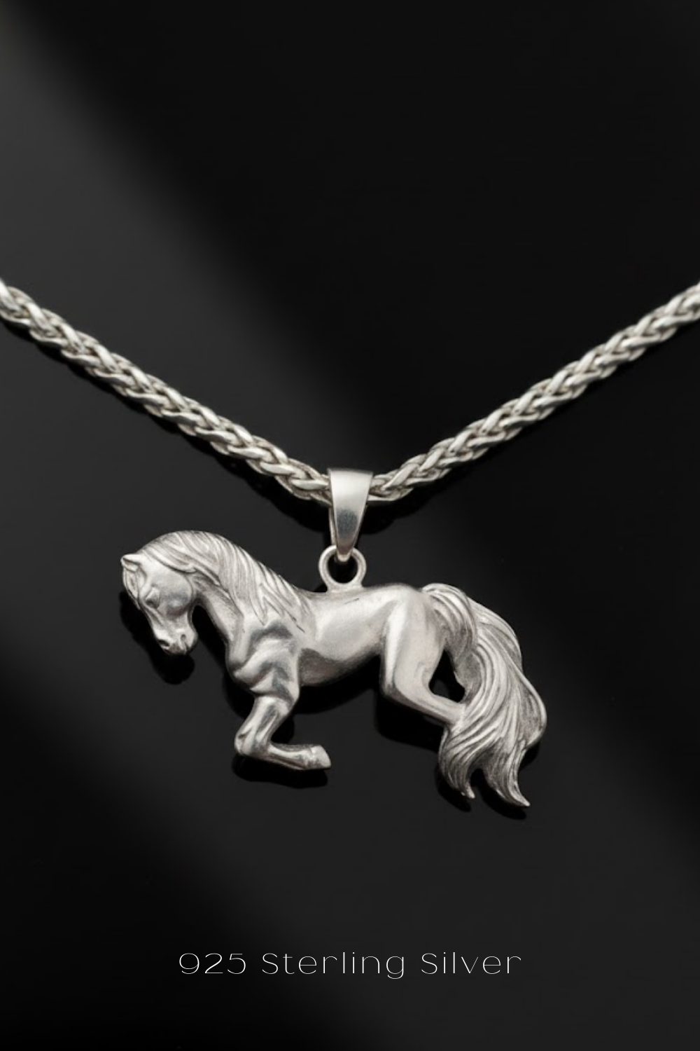 A silver pendant in the shape of a horse is displayed against a black background.