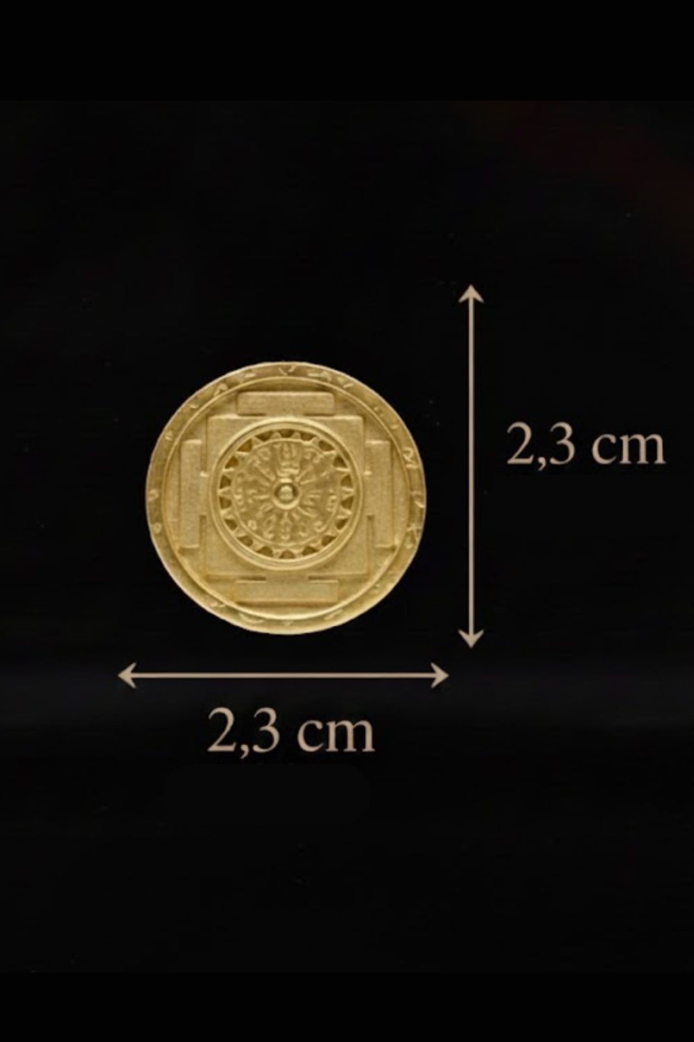 a gold-colored medallion or emblem with a detailed design, placed against a black background. The medallion is approximately 2.3 centimeters in diameter.