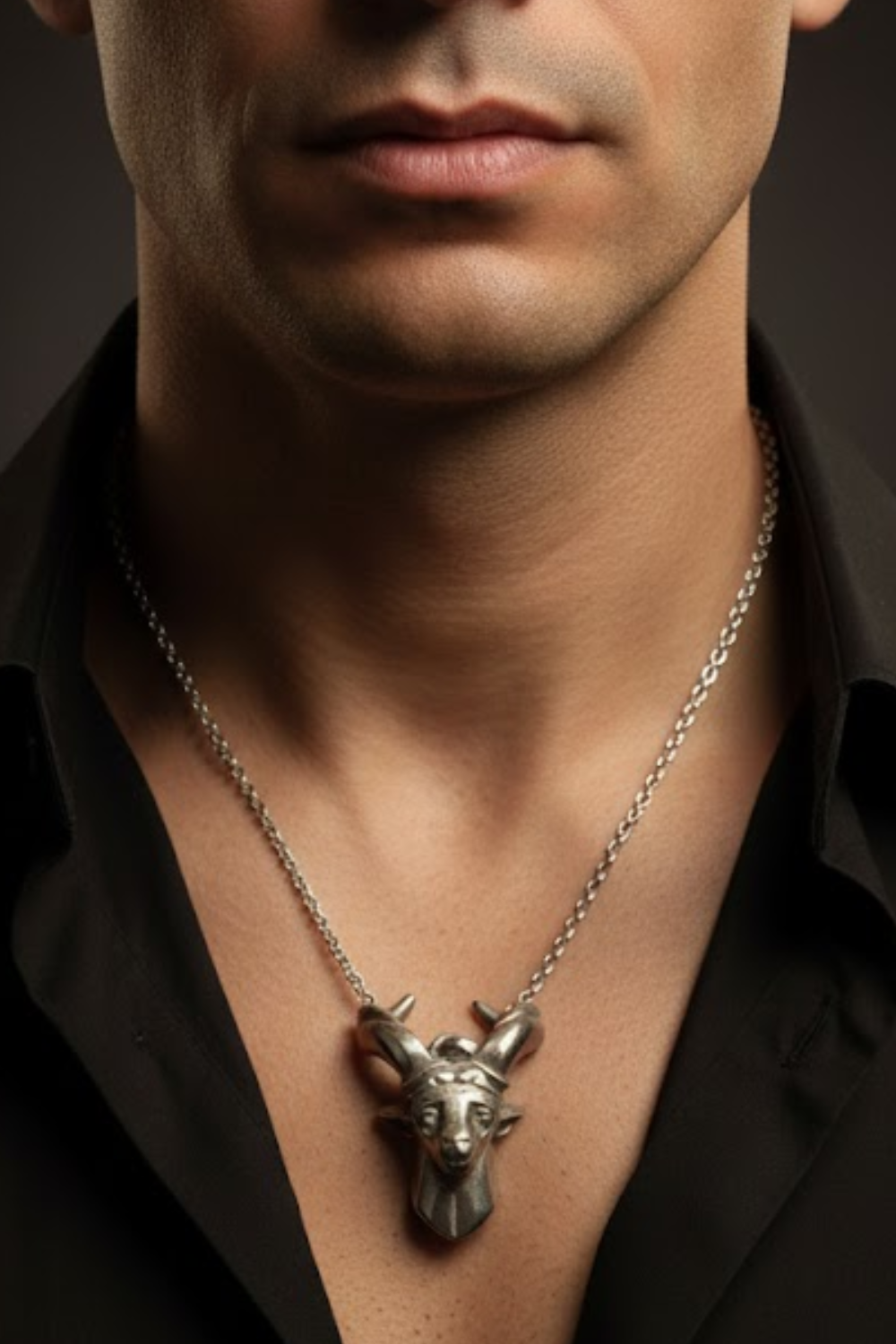 A close-up of a man's neck and chest area, with a silver pendant necklace featuring a goat's head design.