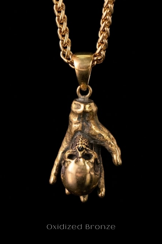 A close-up image of a gold-colored pendant with a skull design, suspended from a chain.