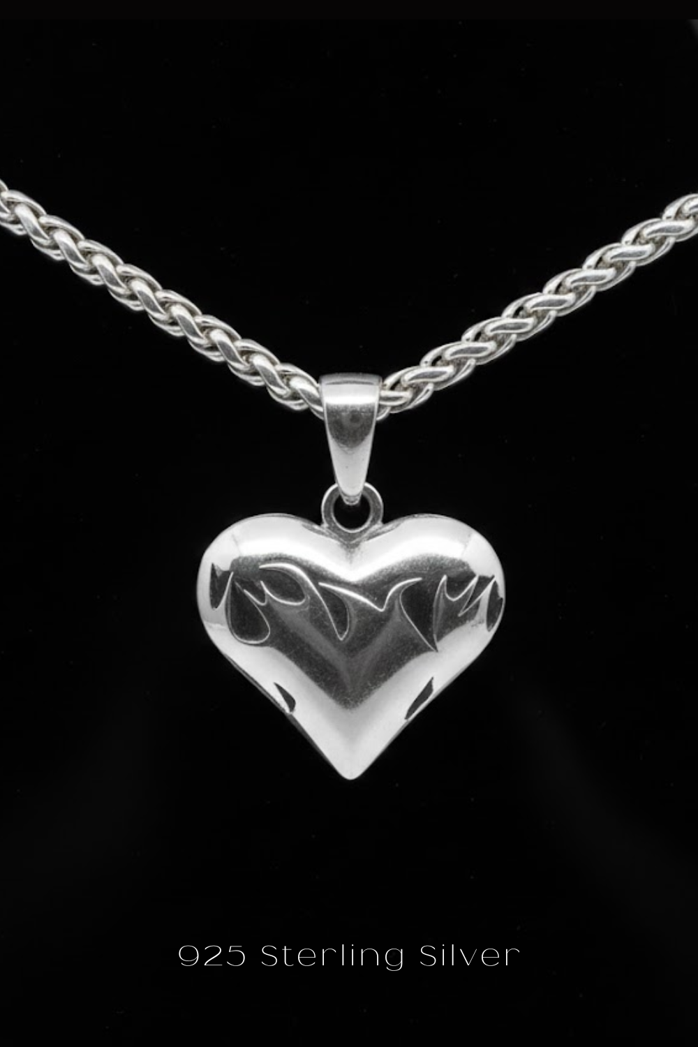 A silver heart-shaped pendant with a chain necklace is displayed against a black background.