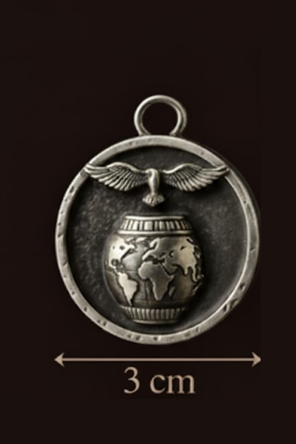 A silver-colored pendant with a globe and a bird in flight, encircled by a metal frame.