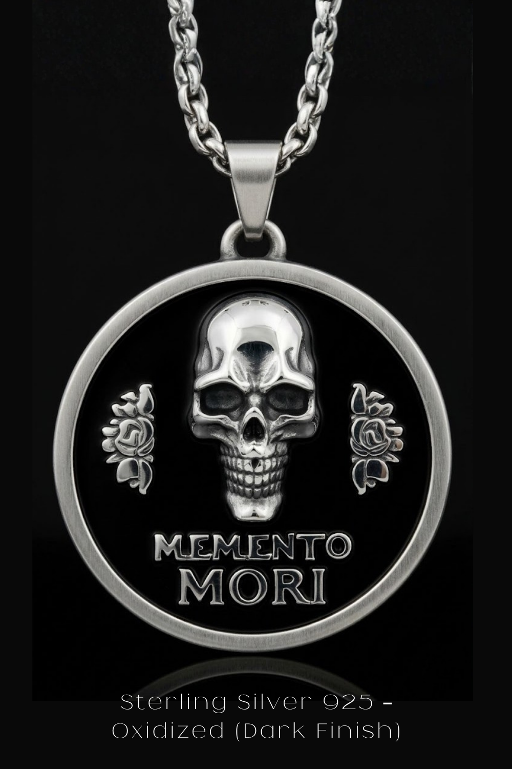 A silver-toned pendant necklace with a circular design featuring a skull and roses, and the text "Memento mori" below the skull.