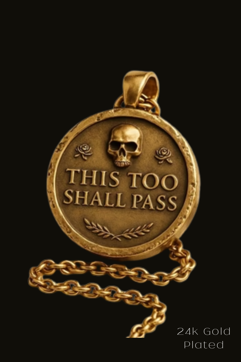 A gold-colored pendant with a skull design and the text "THIS TOO SHALL PASS" engraved on it.