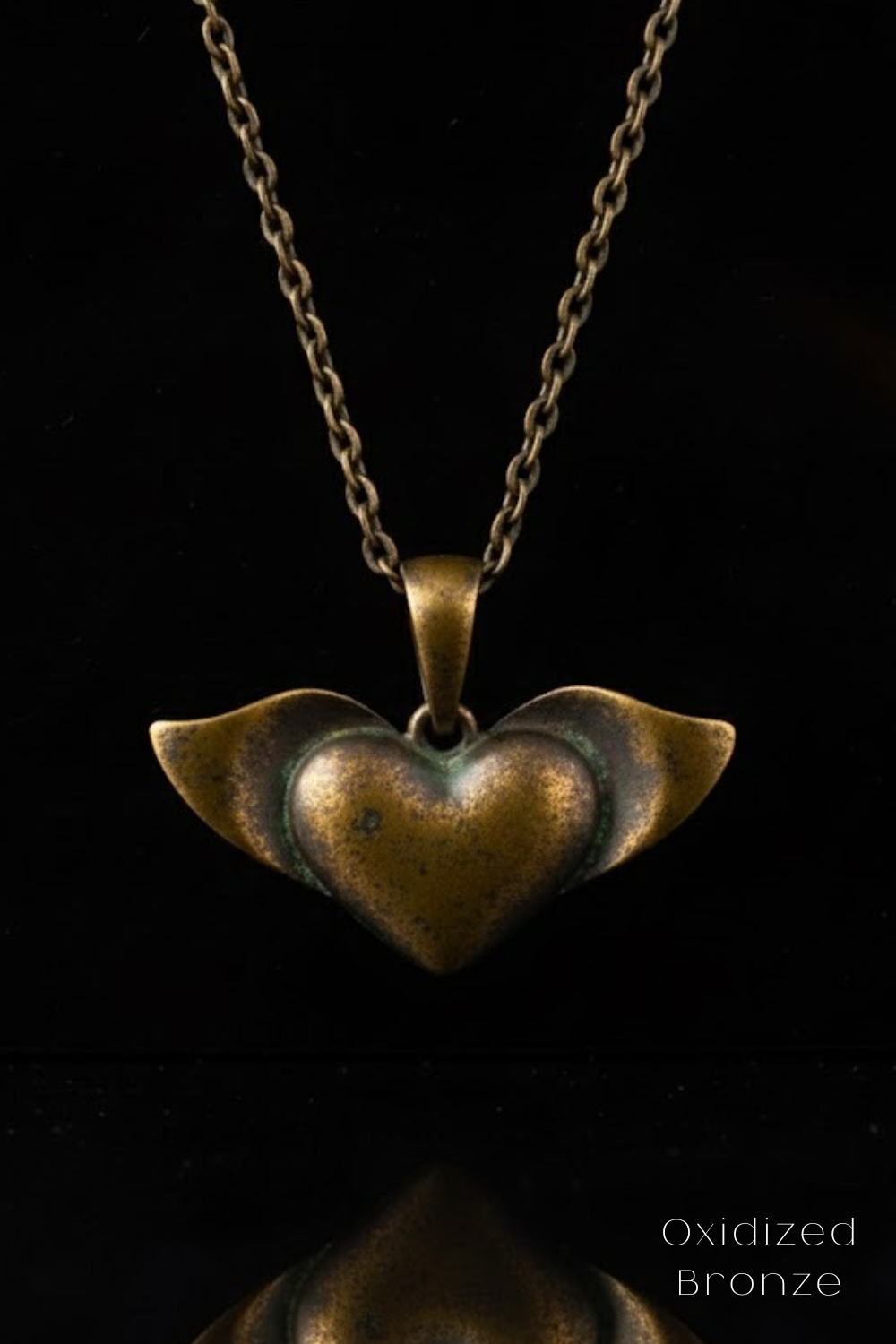 A heart-shaped pendant made of oxidized bronze, suspended from a chain against a black background.