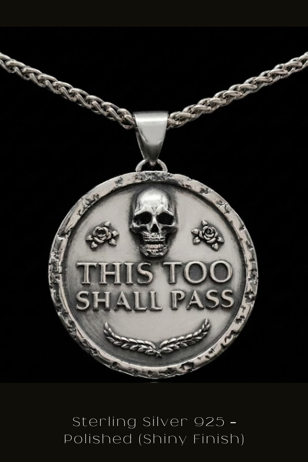 A silver pendant necklace with a circular medallion featuring a skull and the text "THIS TOO SHALL PASS" engraved on it.
