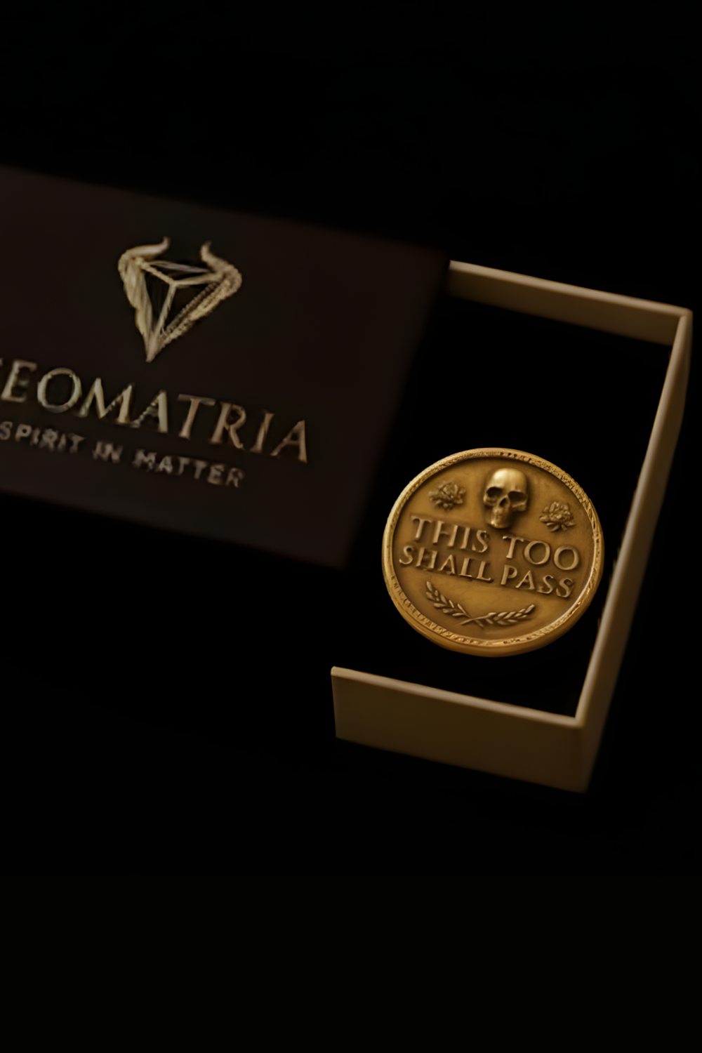 a gold medallion with a skull and laurel wreath design, placed inside a white box with a dark background.