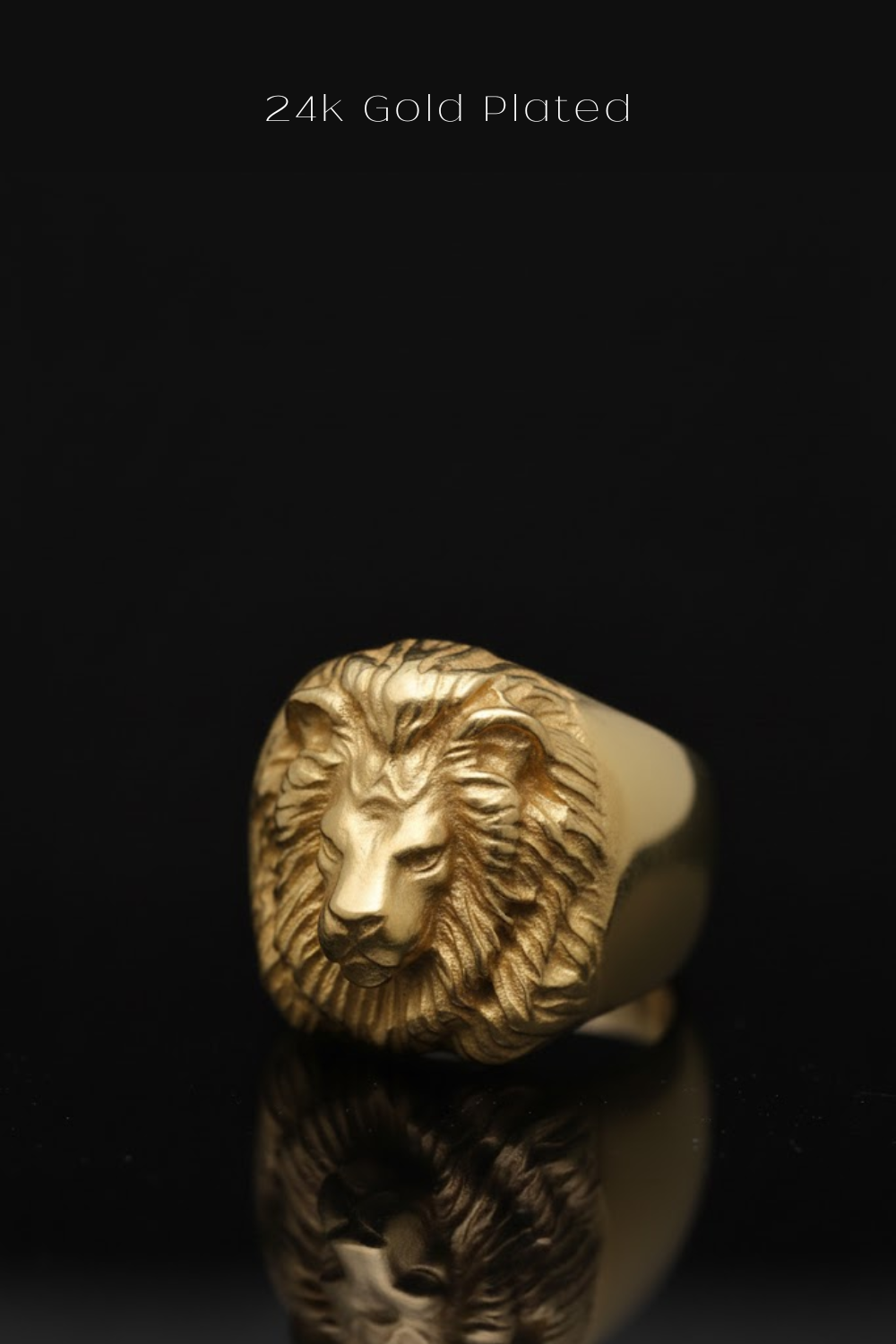 A gold-plated lion head ring is displayed against a black background, with its reflection visible on the surface below.