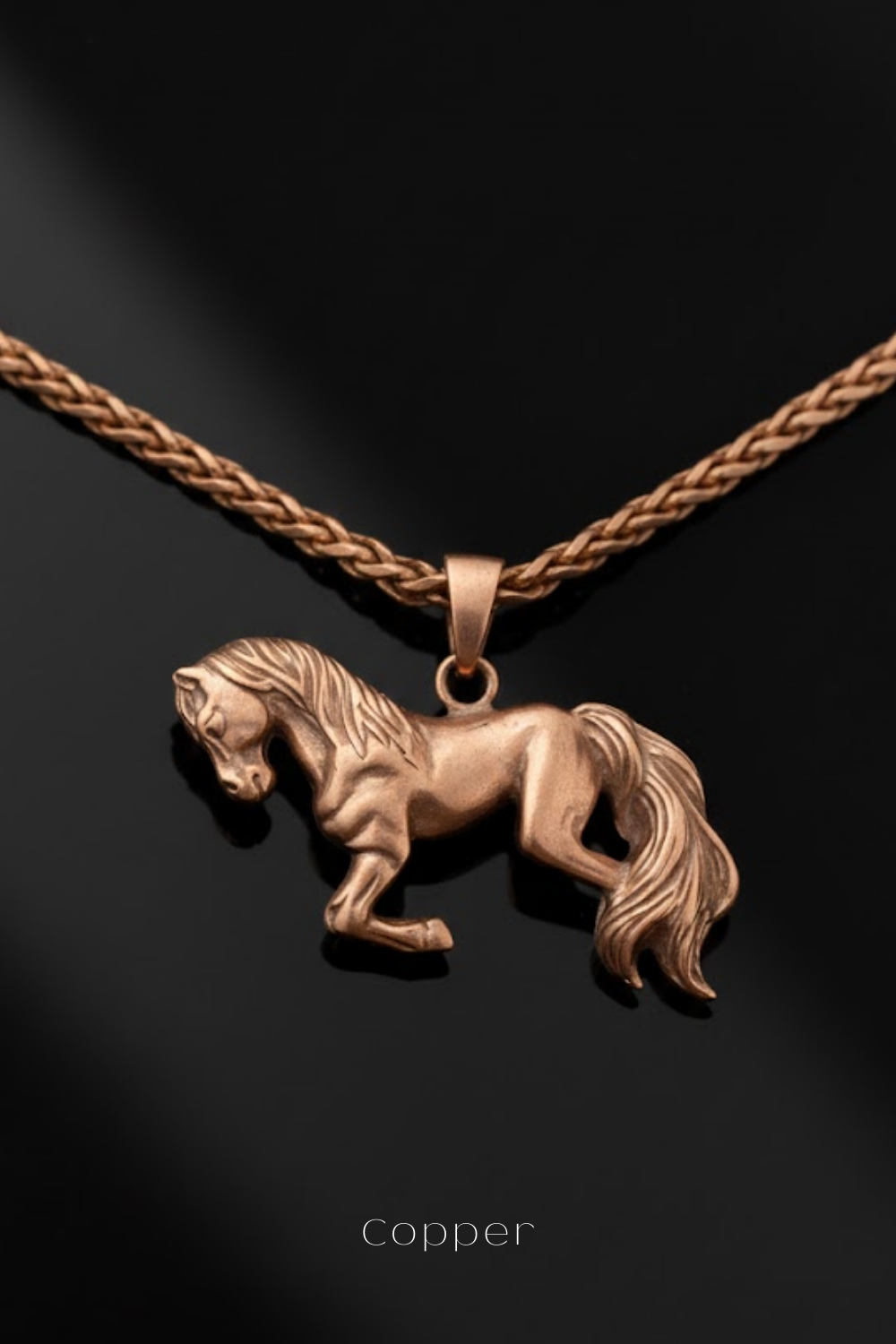 A copper-colored pendant in the shape of a horse is displayed against a dark background, with a braided necklace around it.