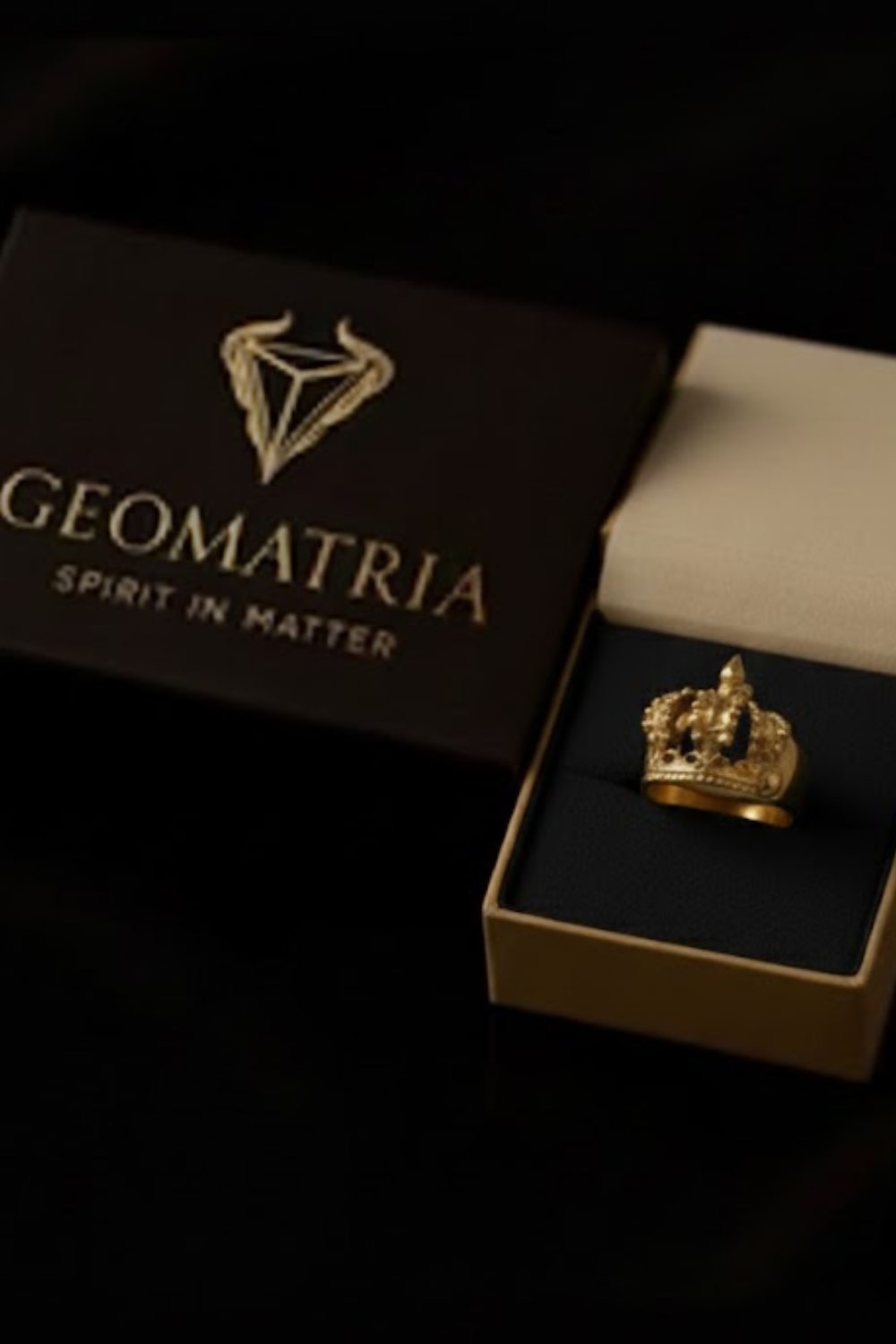A gold crown ring is displayed in a gold box with the text "Geomatria" and "Spirit in Matter" printed on it.