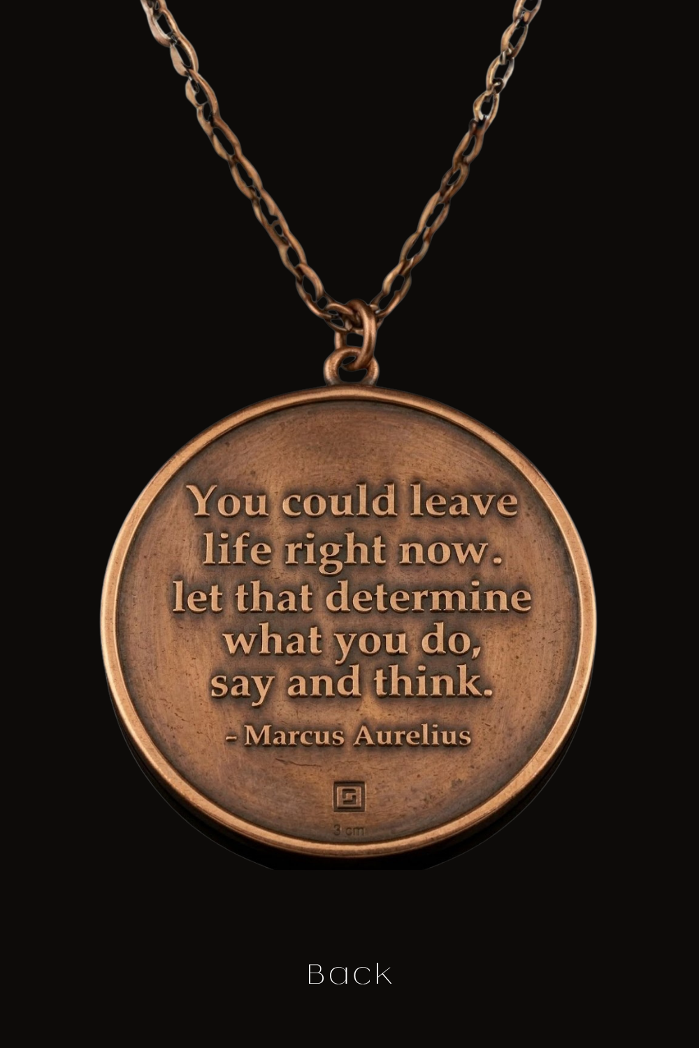 A copper-colored pendant necklace with a quote engraved on it, suspended against a black background.