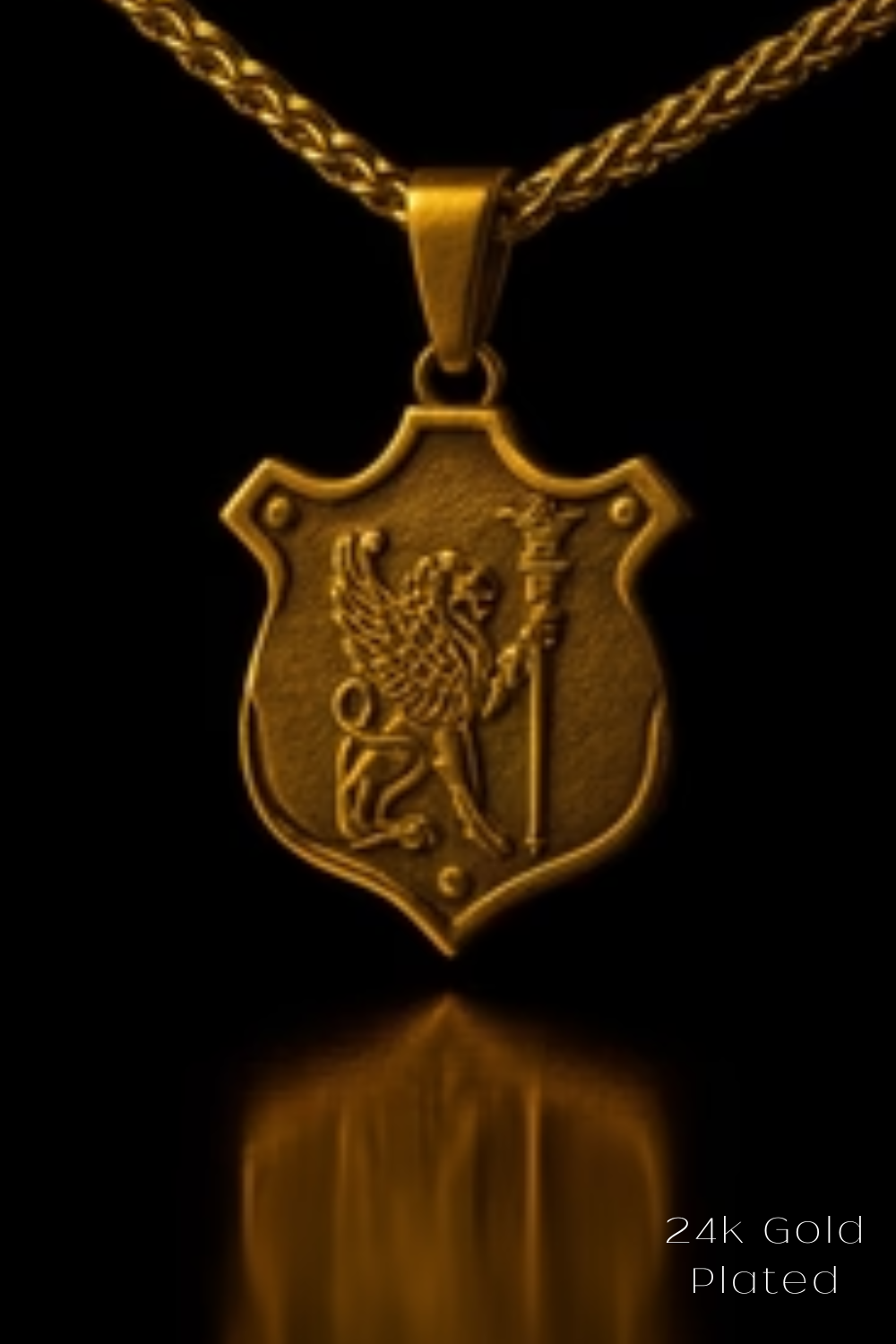 A 24k gold plated pendant featuring a shield-shaped design with a winged lion and a staff, set against a black background.