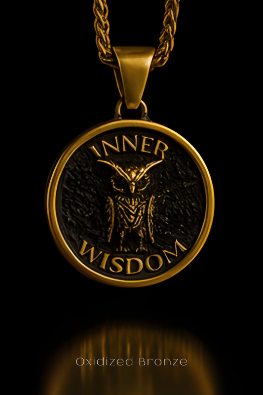 A gold-colored pendant with a black owl design and the words "INNER WISDOM" engraved on it, suspended from a chain against a black background.