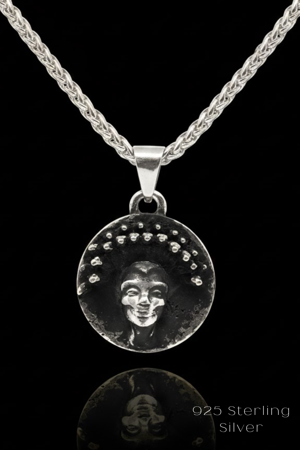 A silver pendant necklace with a circular medallion featuring a face design.