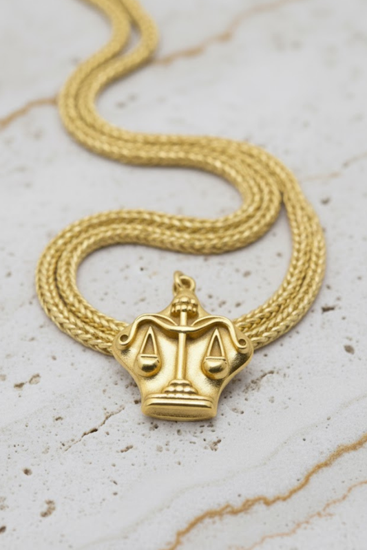 A gold-colored necklace with a pendant in the shape of a scale, symbolizing justice.