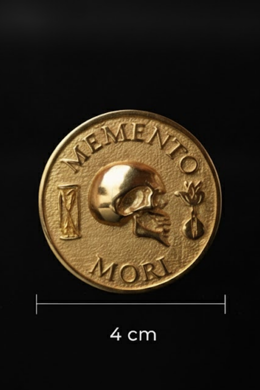 The image is a gold-colored coin with the Latin motto "MEMENTO MORI" (Memento mori) on it.