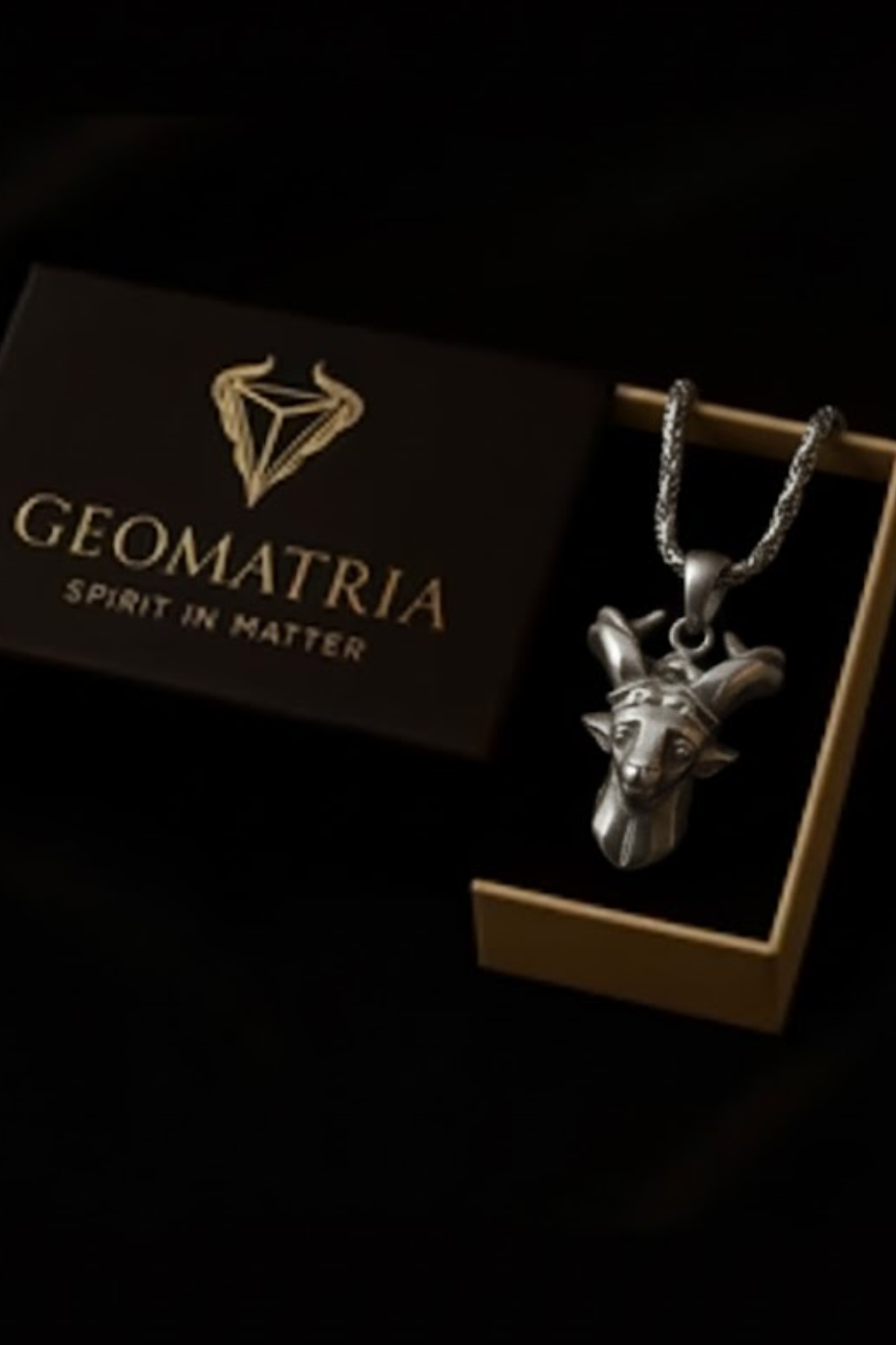 A silver pendant necklace with a geometric design is displayed in a wooden box with the text "Geomatria Spirit in Matter" printed on it.