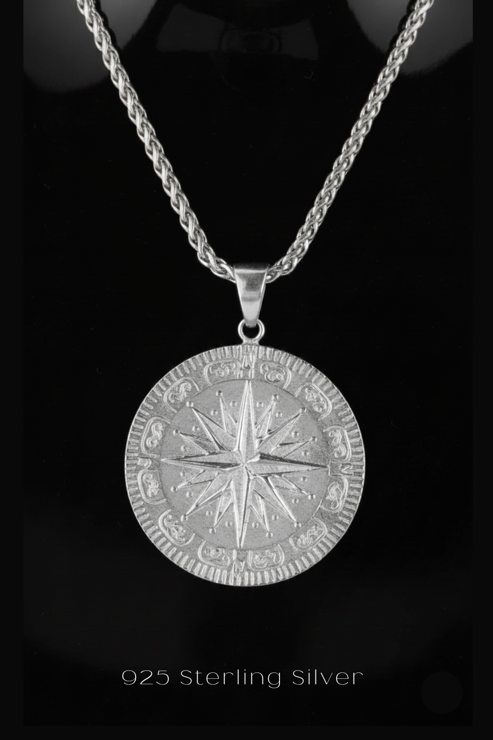 A silver-colored pendant necklace with a round medallion featuring a compass design.