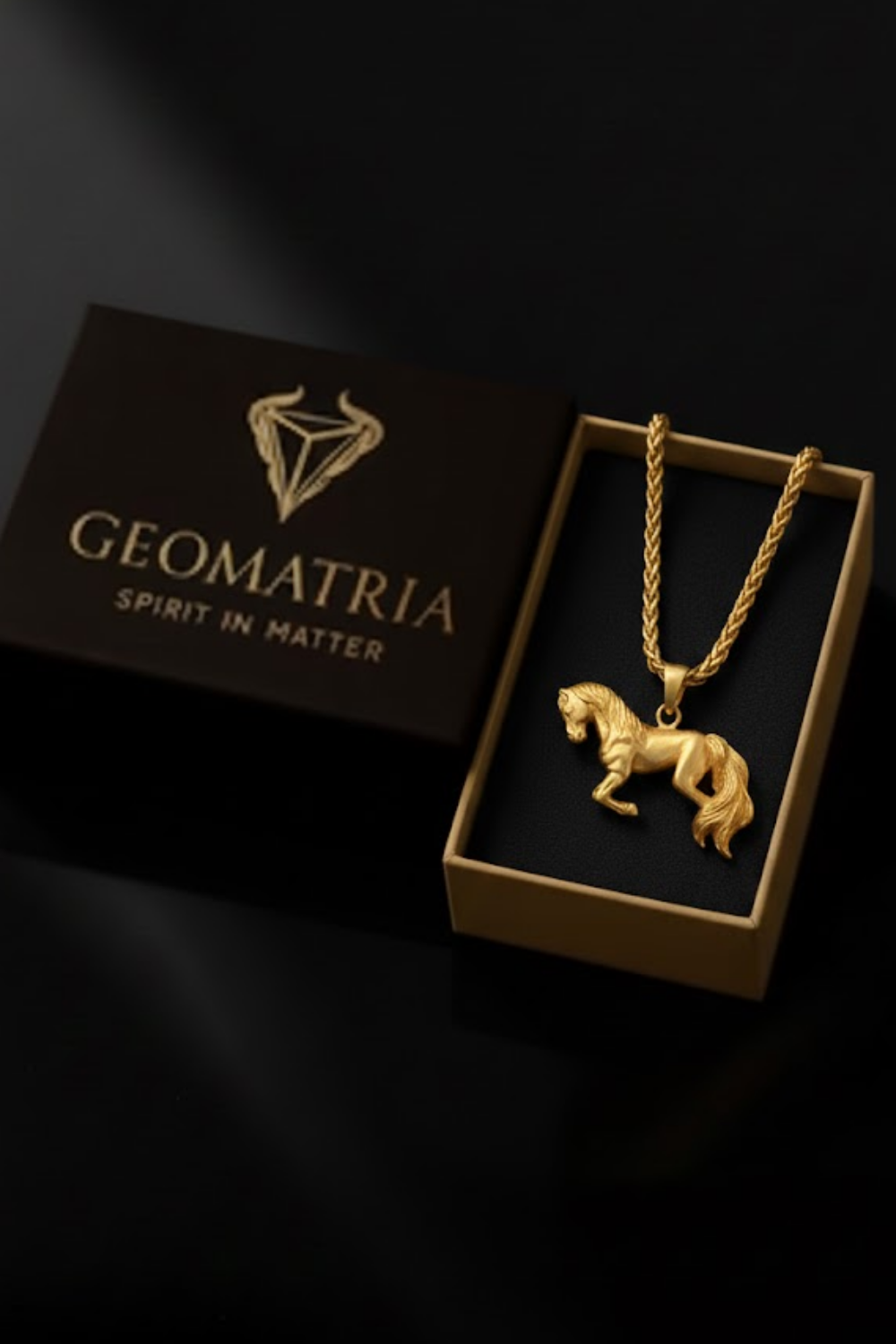 A gold-colored necklace with a pendant in the shape of a horse is displayed in a black box with the Geomatria logo.