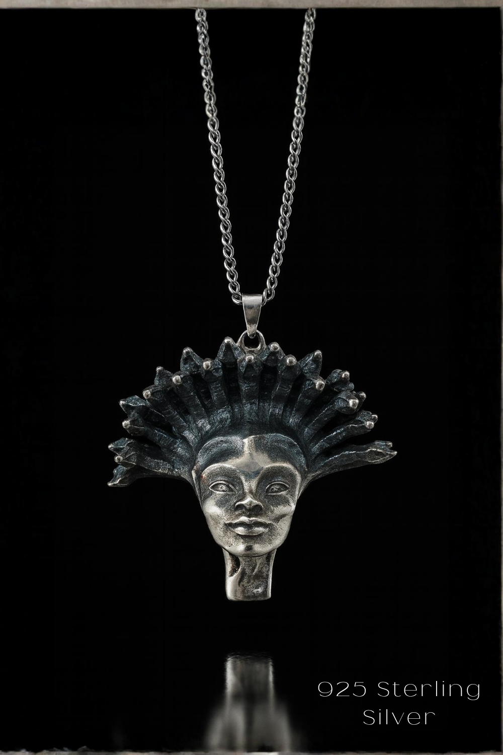 A silver pendant necklace with a detailed, intricate design featuring a stylized female face or profile.