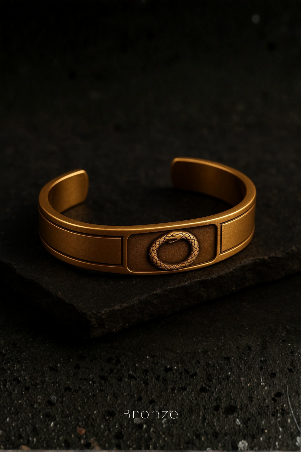 A gold-colored bracelet with a snake design on the front rests on a dark surface.