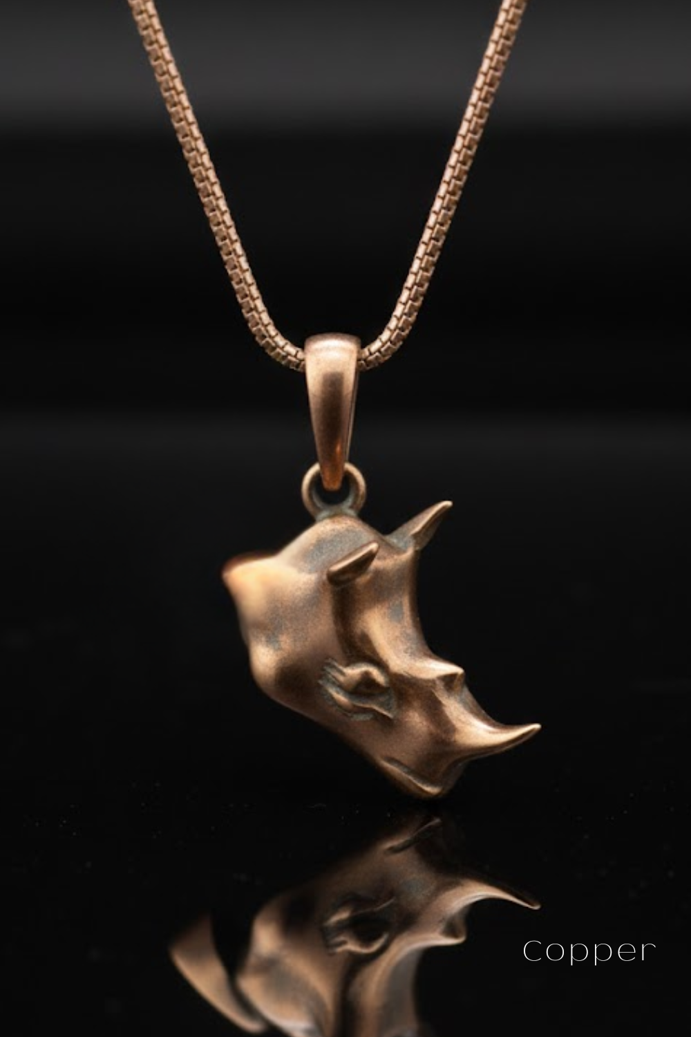 A copper-colored pendant necklace with a unique, sculpted design hanging against a black background.