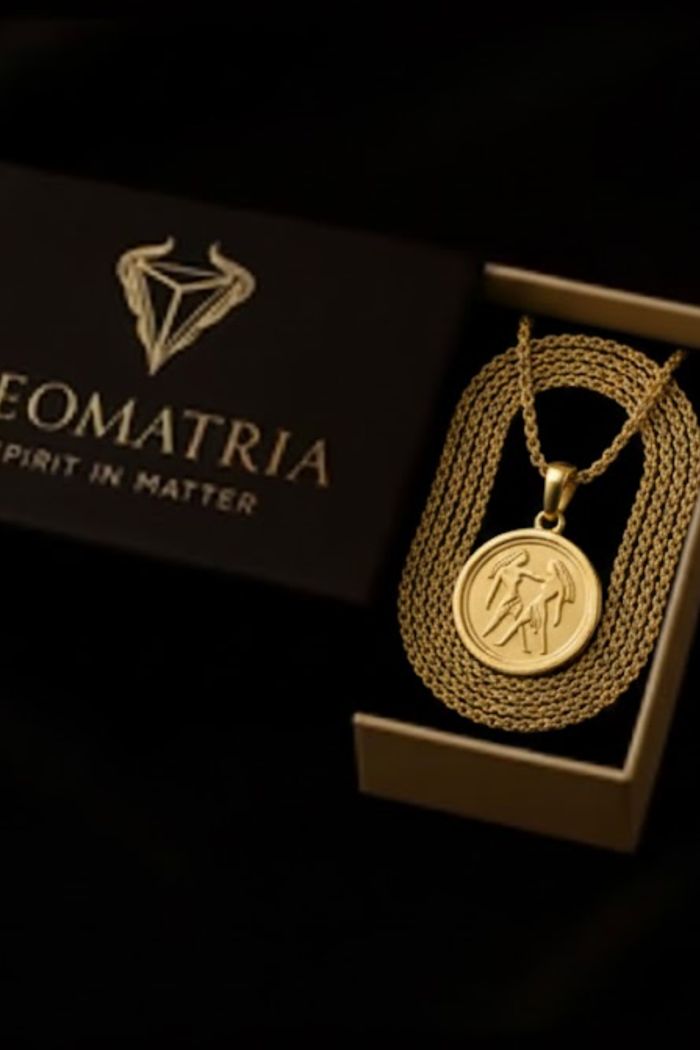 a gold necklace with a pendant, displayed in a black box with the text "Geomatria" printed on it.