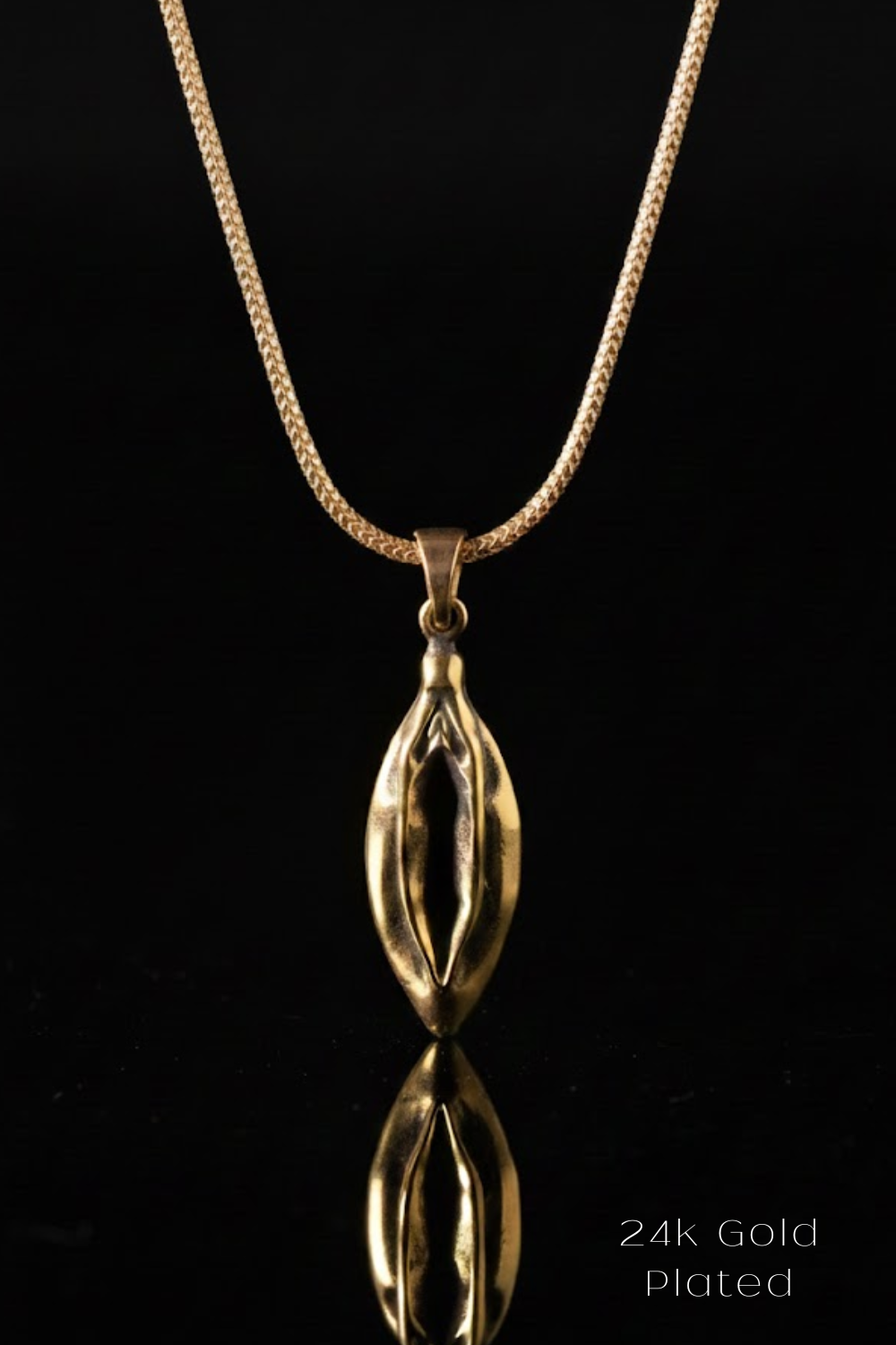 A gold-plated pendant necklace with a unique, sculpted design is displayed against a black background.