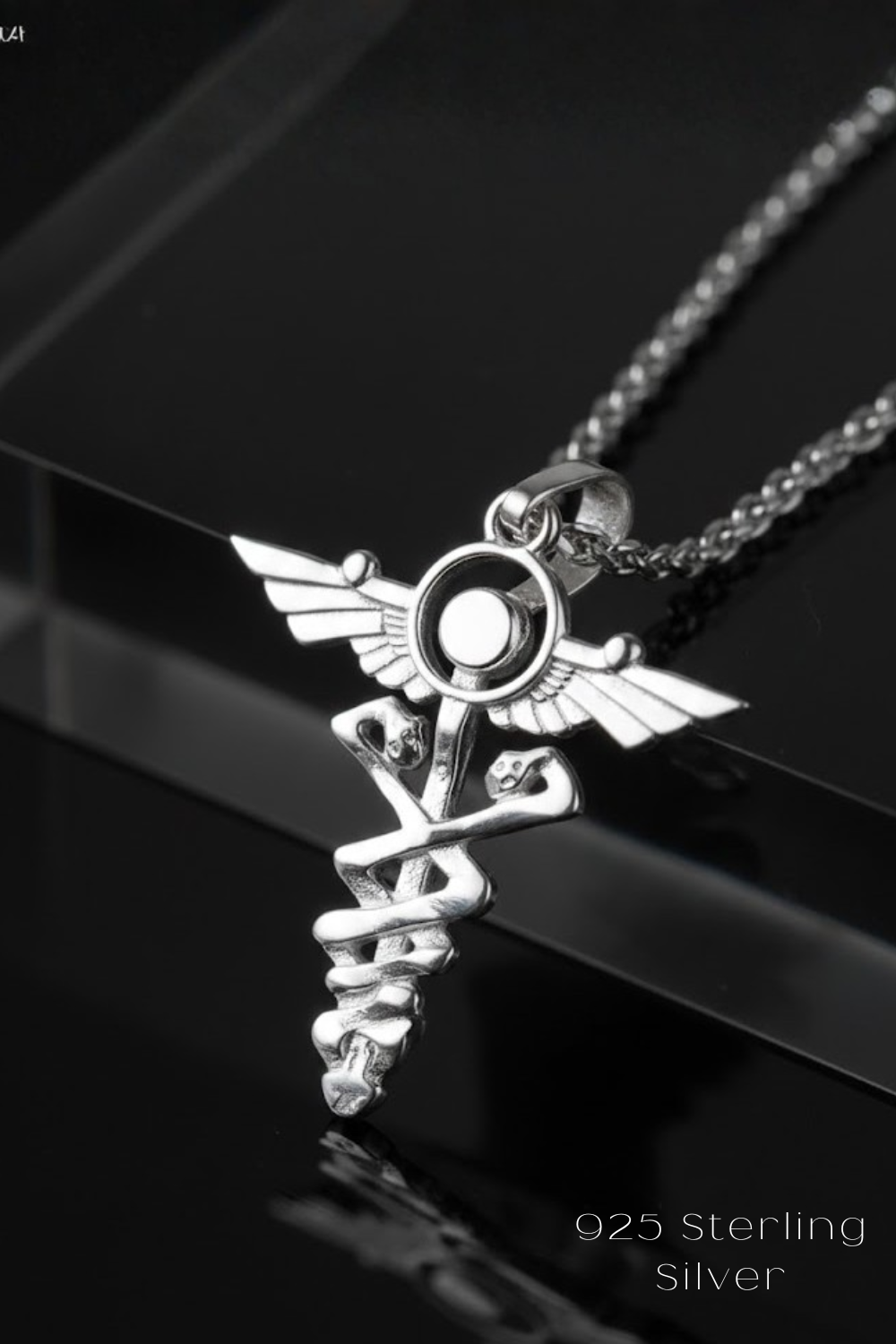 A silver medical symbol pendant with wings and a cross is displayed on a chain against a black background.