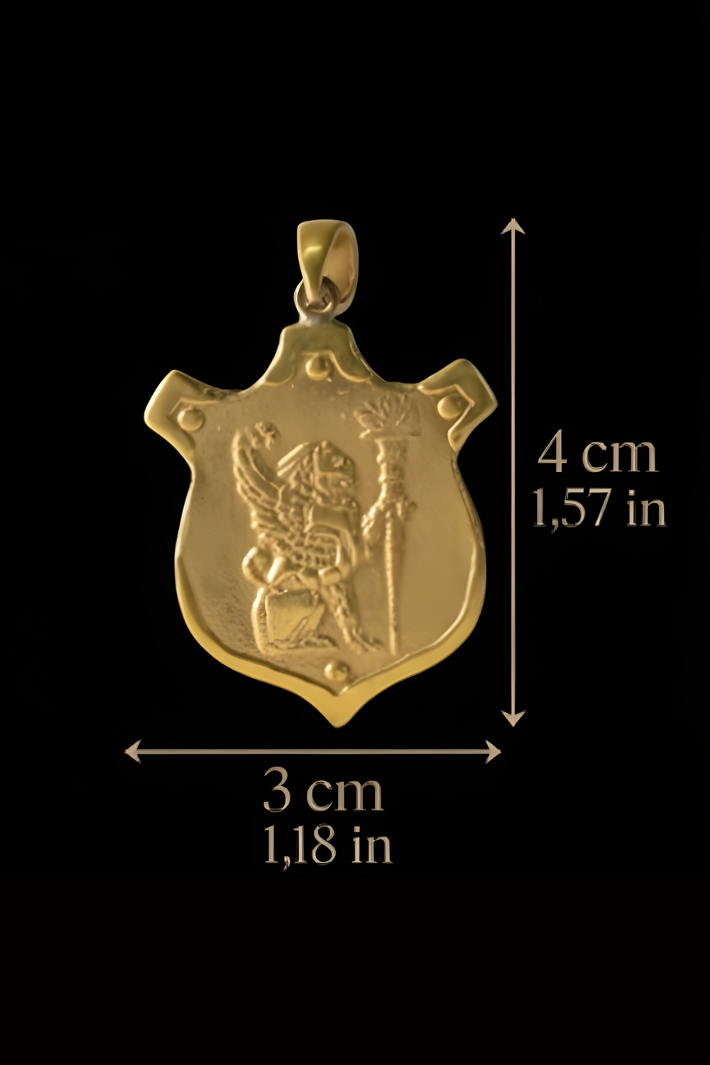 A gold-colored pendant with a shield-shaped design, featuring a figure holding a staff. The pendant is described as being 4 cm in length and 1,58 cm in width.