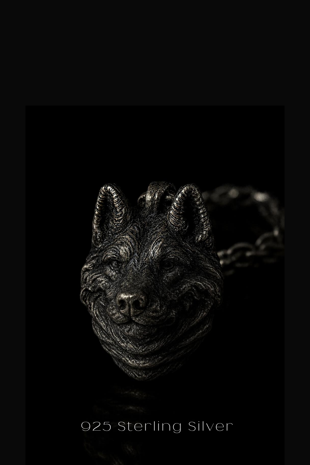 A close-up of a silver wolf pendant against a black background.