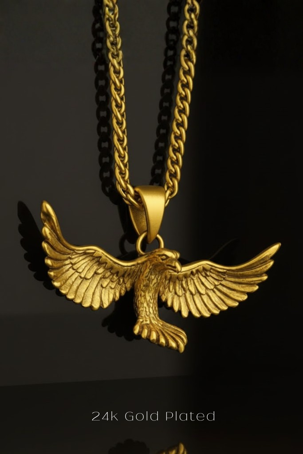 A gold-plated pendant in the shape of a soaring eagle, with wings spread wide, is displayed against a black background.