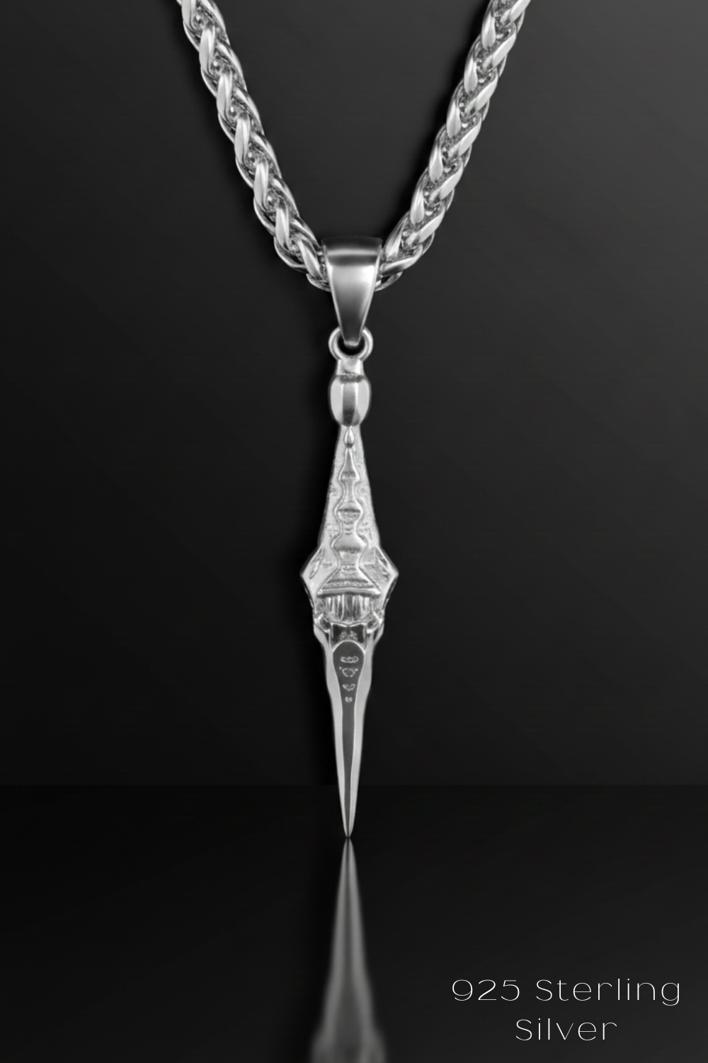 A silver necklace with a pendant featuring an intricate design, displayed against a black background.