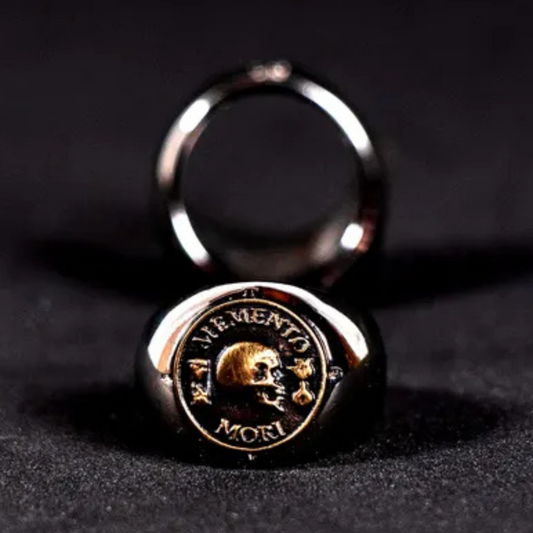a close-up of a ring with a skull design and the Latin phrase "VIMENTO MORI" inscribed on it.