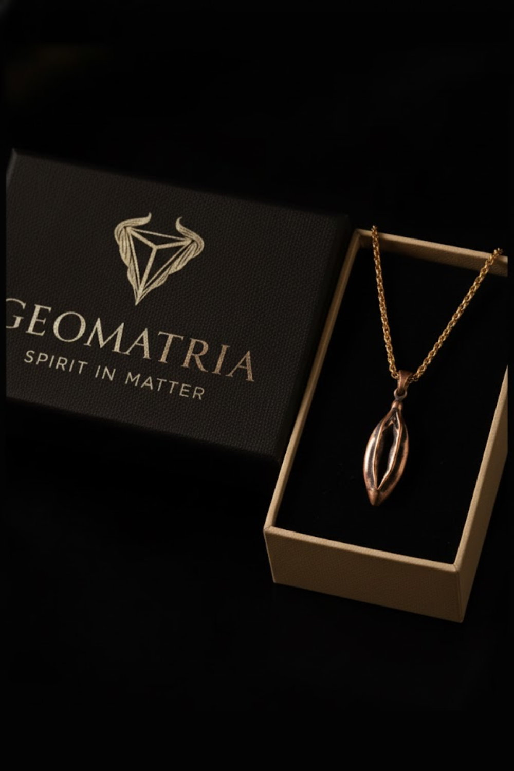 A gold necklace with a pendant is displayed in a black box with the text "Geomatria Spirit in Matter" printed on it.