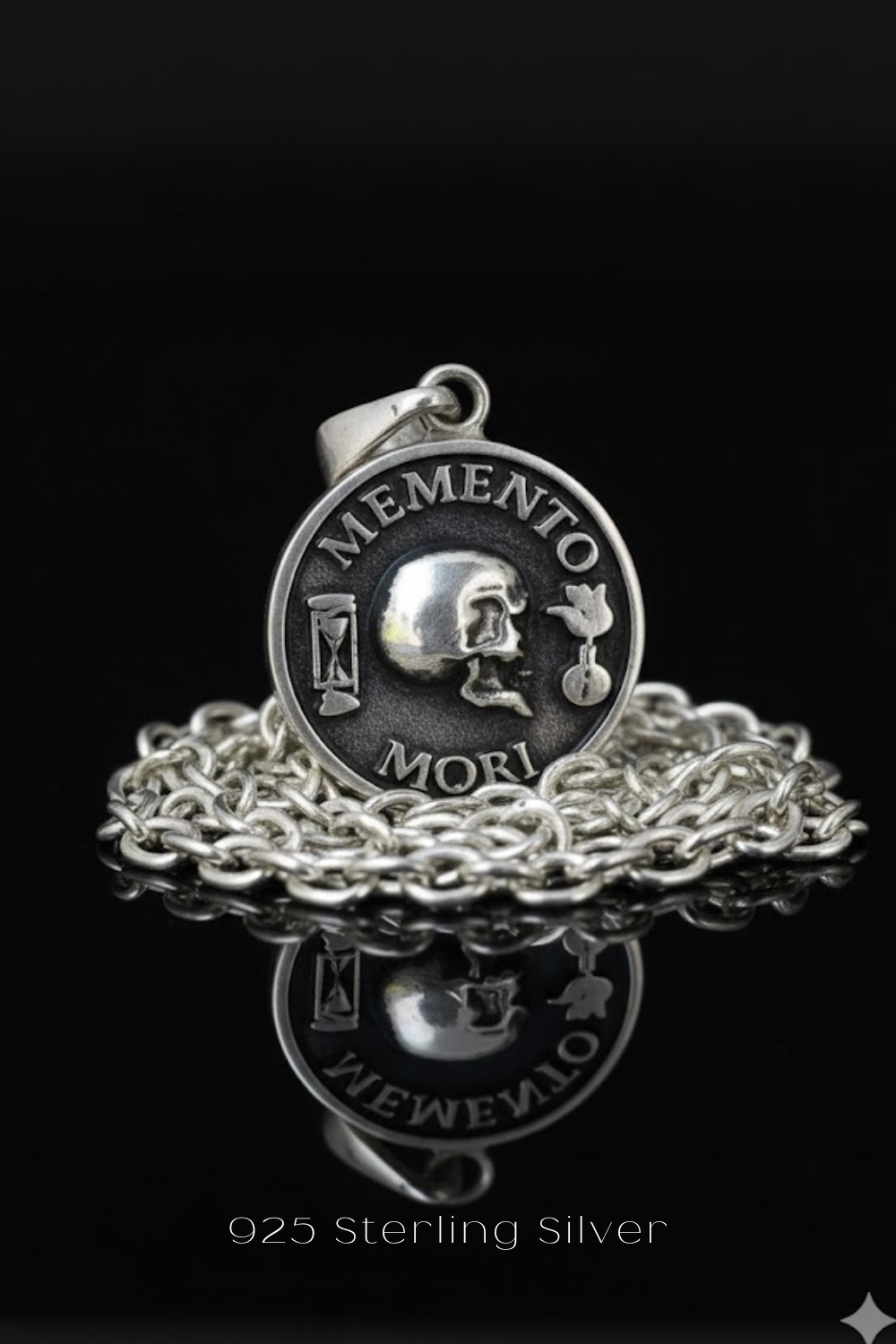 A silver-colored pendant with the Latin motto "Memento mori" engraved on it, which means "Remembering the dead" in English. The pendant is displayed on a chain against a black background.