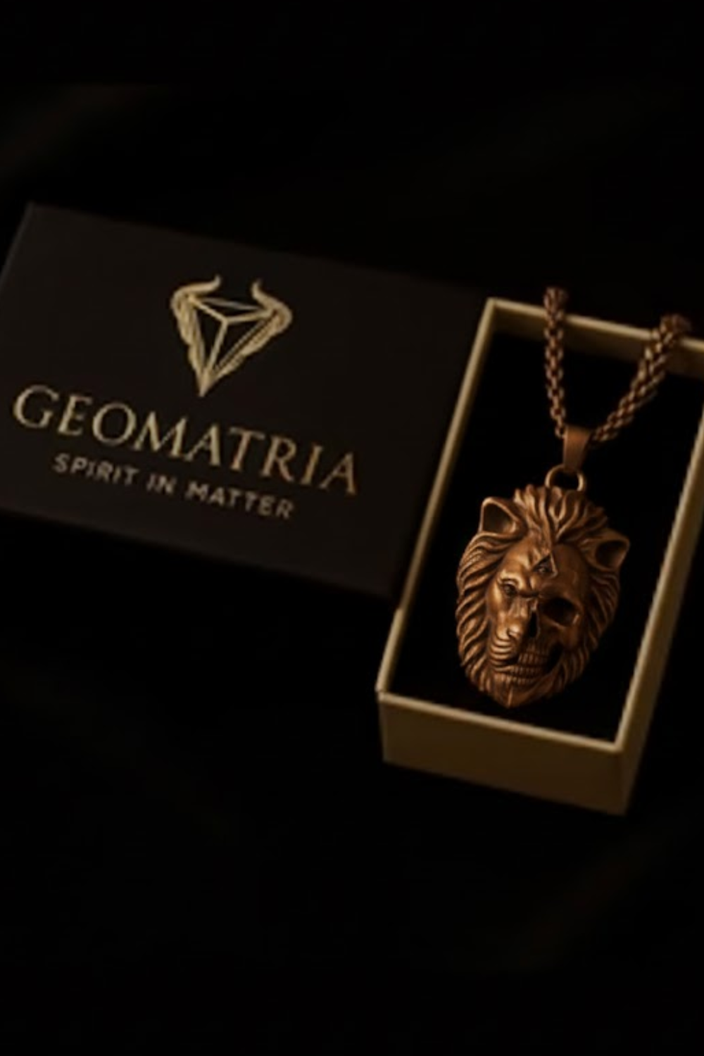 A pendant in the shape of a lion's head is displayed in a box with the text "Geomatria" and "SPIRIT IN MATERIA" printed on it.