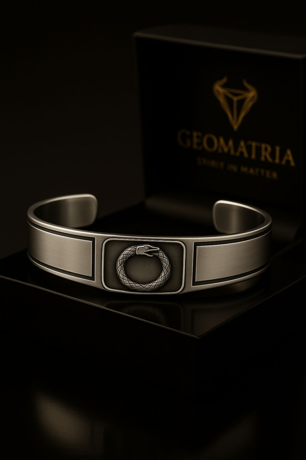A silver bracelet with a geometric design sits on a black surface, with a black box featuring a gold logo in the background.