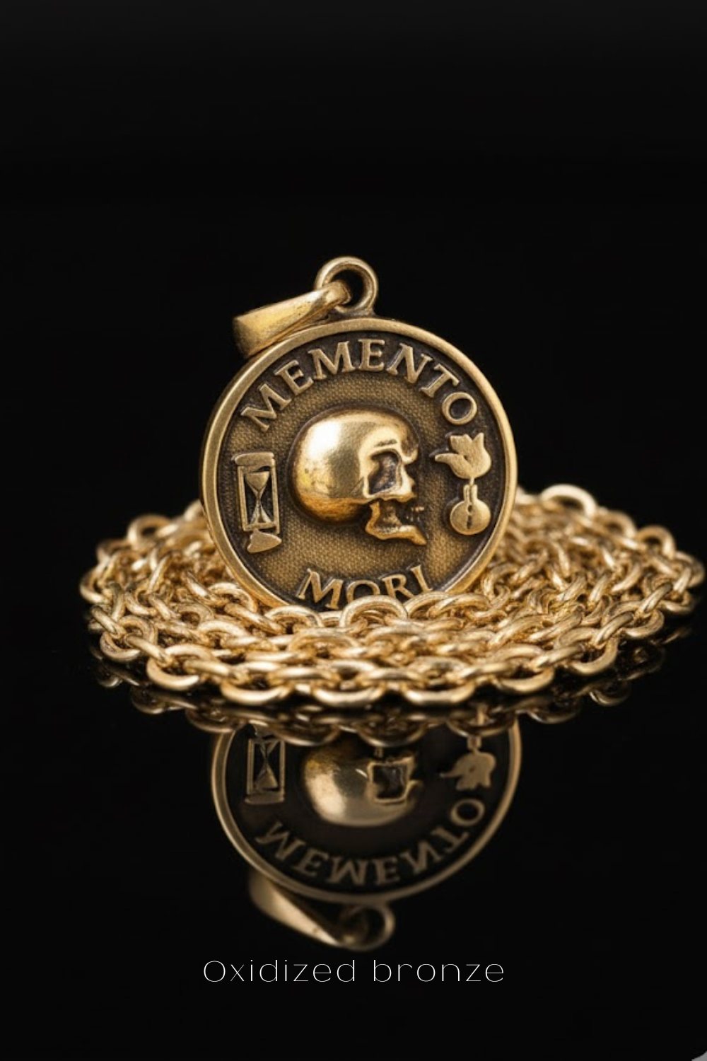 a gold-colored pendant with a skull design, surrounded by a chain and placed on a reflective surface.