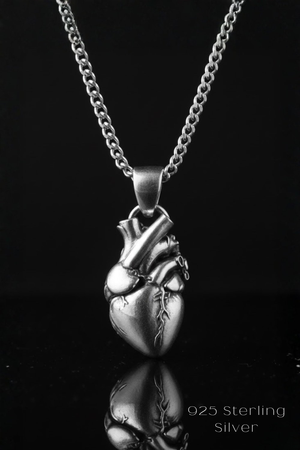 A silver-colored pendant necklace with a heart-shaped pendant is displayed against a black background.